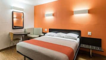 A hotel room with a bed, a desk, a chair, and a mirror.