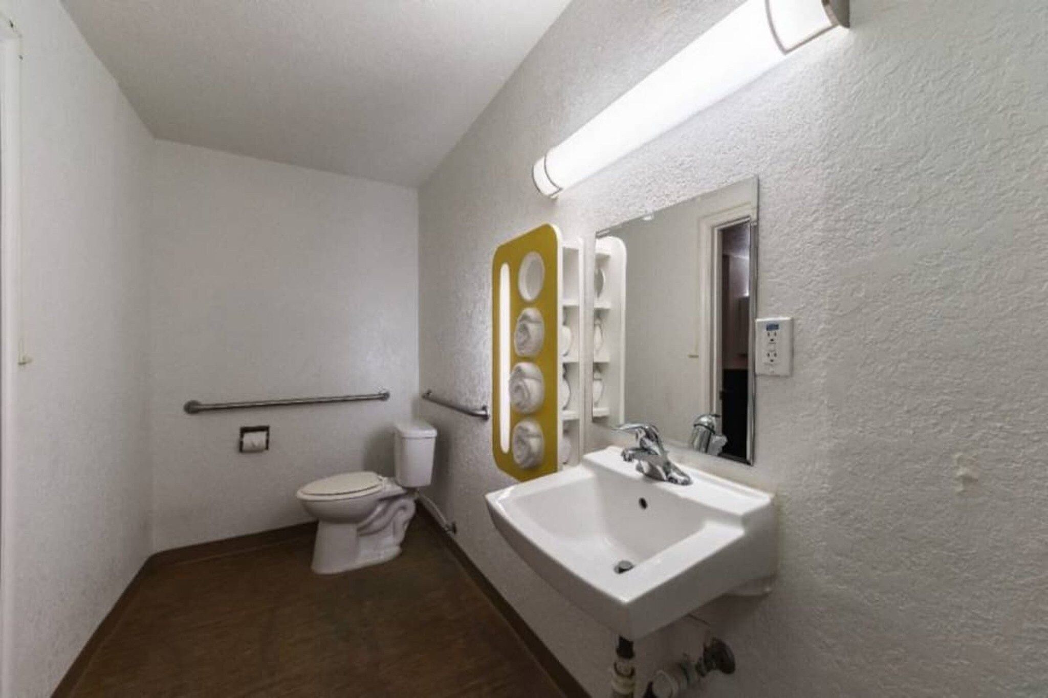A small bathroom with a toilet, sink, mirror, and a handrail.