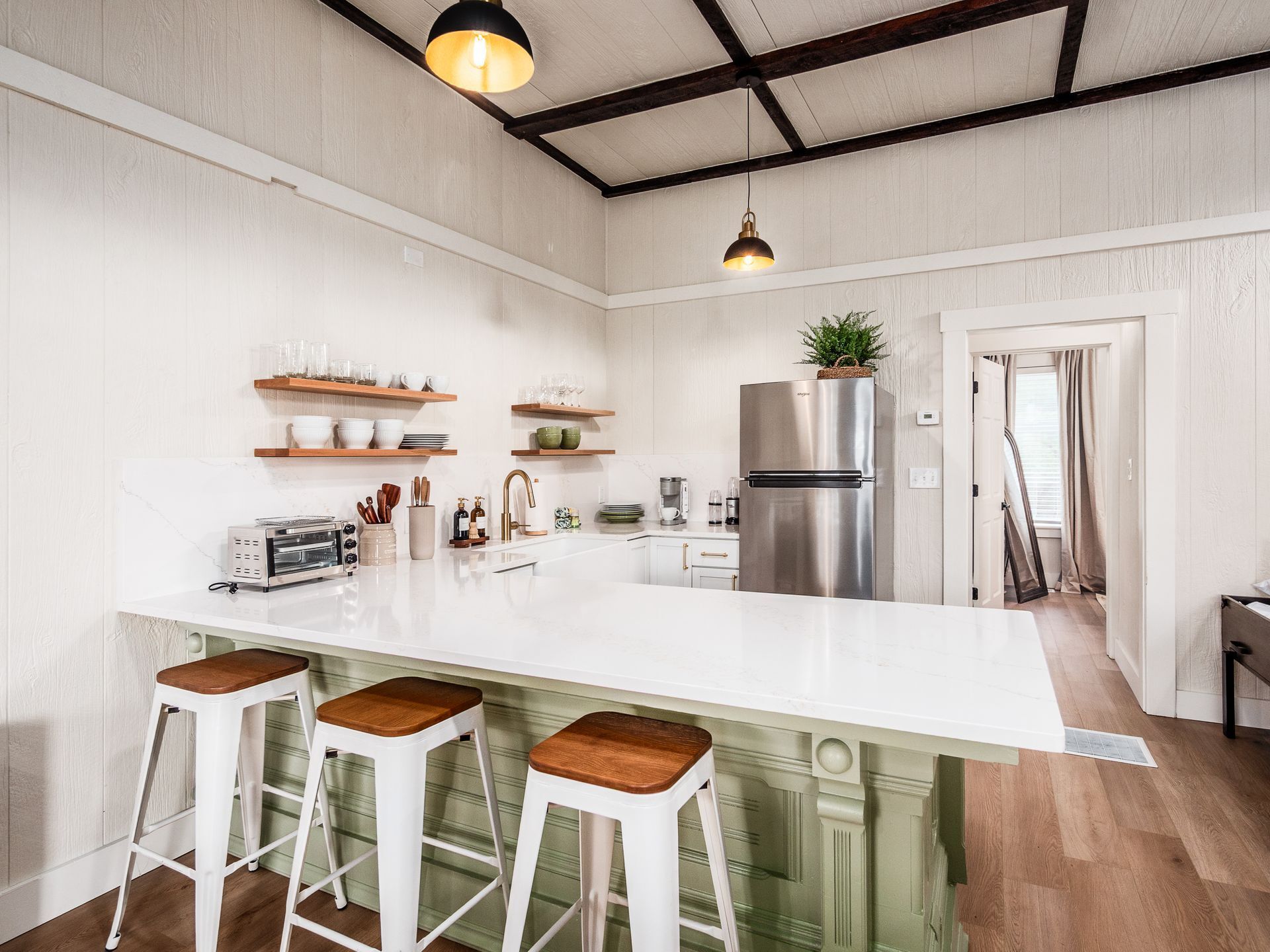 Une cuisine moderne dotée d’un grand îlot central, de tabourets de bar, d’un réfrigérateur et de poutres en bois au plafond.
