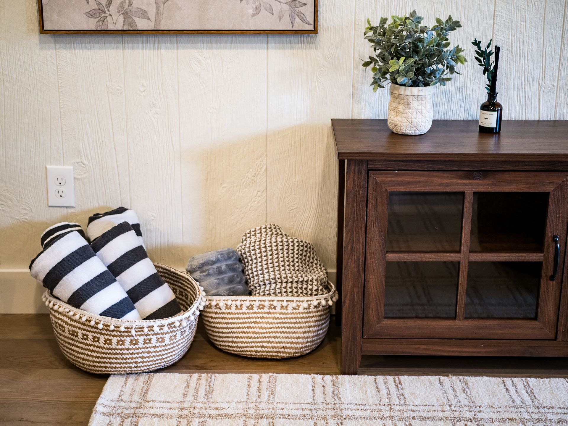 Una habitación con un armario de madera, dos cestas tejidas y una planta en maceta sobre una mesa de madera.