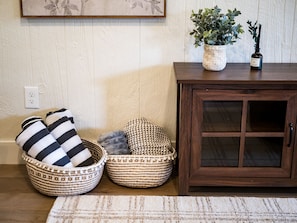 Una habitación con un armario de madera, dos cestas tejidas y una planta en maceta sobre una mesa de madera.