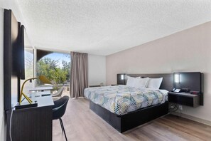 Habitación de hotel con cama, mesita de noche, escritorio, silla y vistas al exterior.
