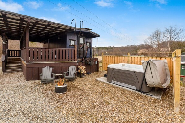 A covered outdoor area with a hot tub, Adirondack chairs, and a fire pit. - The Caboose | Hocking Hills, Hot Tub, Pickleball (Creola)