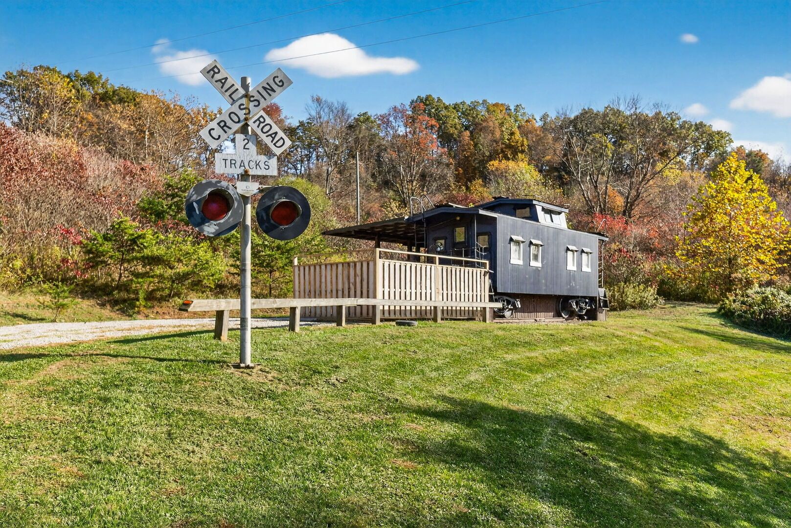 A railroad crossing sign with two tracks, a wooden fence, and a small building with a shed roof.