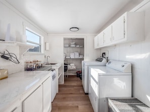 A compact laundry room with a washing machine, dryer, and shelves for folded clothes. - The Caboose | Hocking Hills, Hot Tub, Pickleball (Creola)