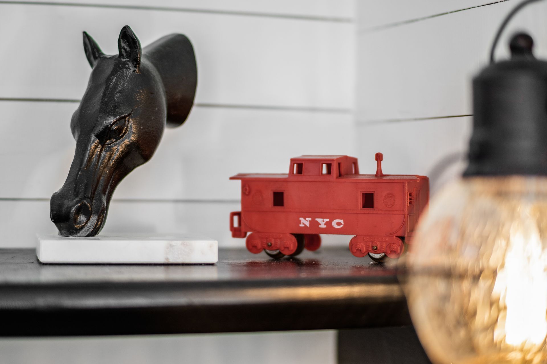 Eine Skulptur eines Pferdekopfes, ein rotes Modell eines New Yorker Zugwagens und eine Glühbirne auf einem Regal.