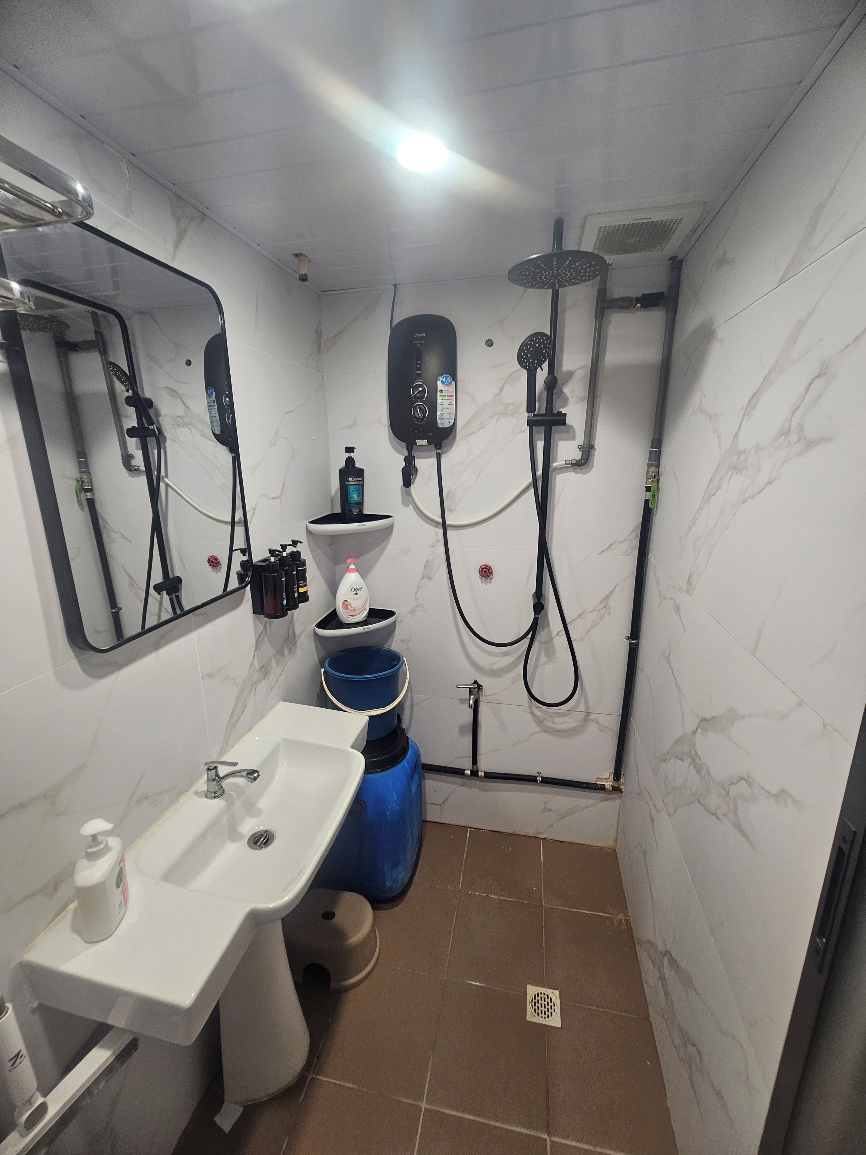 Une petite salle de bain avec un lavabo blanc, un miroir, une douche et des toilettes.