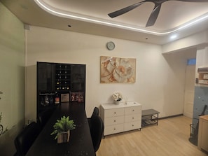 Un comedor moderno con una mesa larga, sillas, una planta en maceta, una estantería para vinos y un adorno en la pared.
