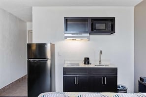 A compact kitchenette with a refrigerator, microwave, and a sink with a faucet.