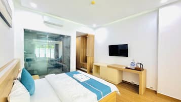 A hotel room with a bed, a desk, a TV, and a glass shower enclosure.