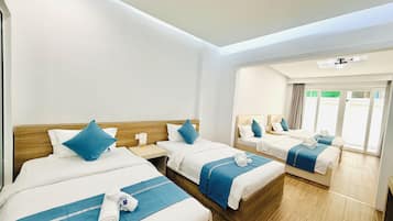 Een hotelkamer met twee bedden, elk met een houten hoofdbord, wit beddengoed en blauwe accenten. Er staan twee nachtkastjes met lampen bij, en de kamer heeft een grote schuifdeur naar een buitenruimte.