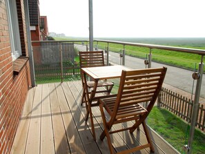 Eine Holzterrasse mit Tisch und Stühlen, mit Blick auf eine Straße und Grünflächen.