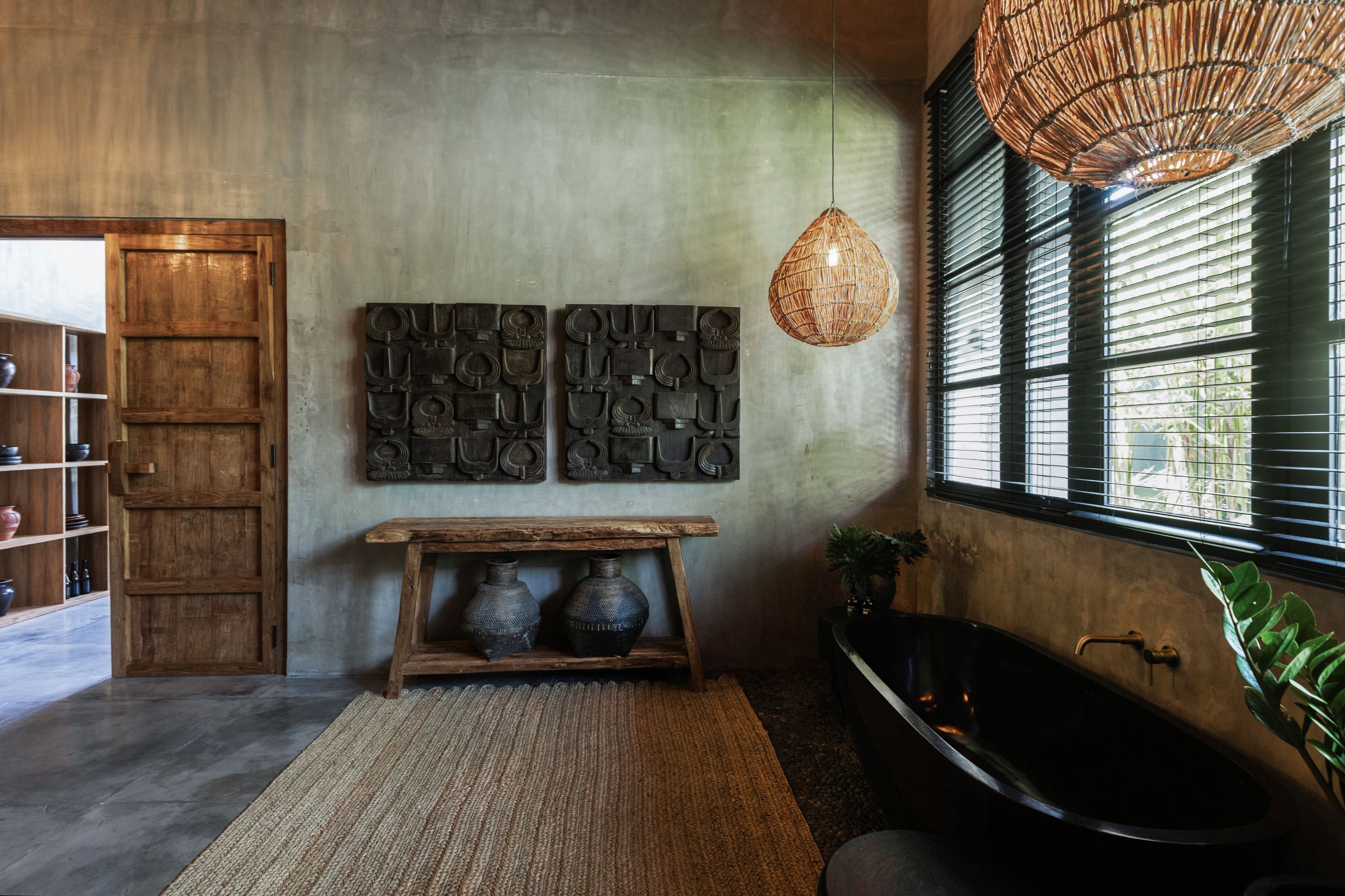 A bathroom with a black bathtub, a woven rattan light fixture, and a wall-mounted decorative panel.