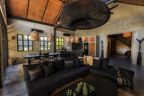 A spacious living area with a large black sectional sofa, a dining table, and a kitchen in the background. - Villa Sen Zen Seminyak (Seminyak)