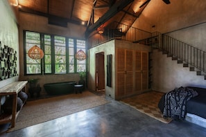 Um quarto amplo com uma janela grande, uma escada e um espaço de estar com um banco e uma mesa.