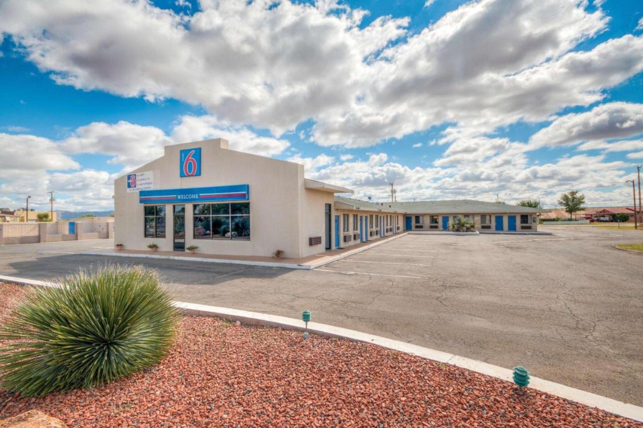A motel with a '6' sign, a 'Welcome' banner, and a parking lot.