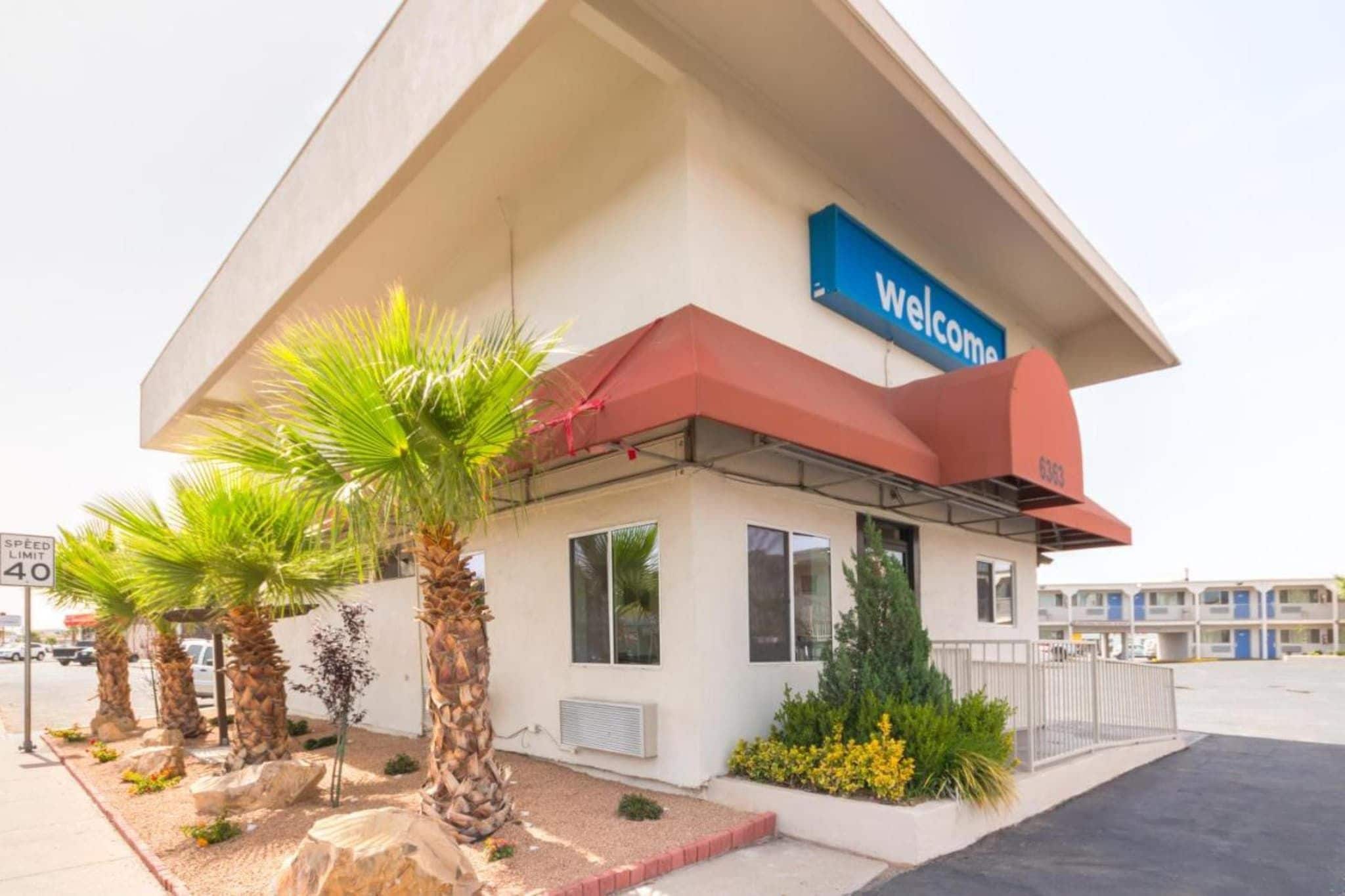 A building with a 'Welcome' sign, palm trees, and a speed limit sign.