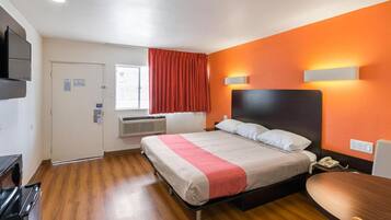 A hotel room with a bed, a desk, a chair, a television, and a window with curtains.