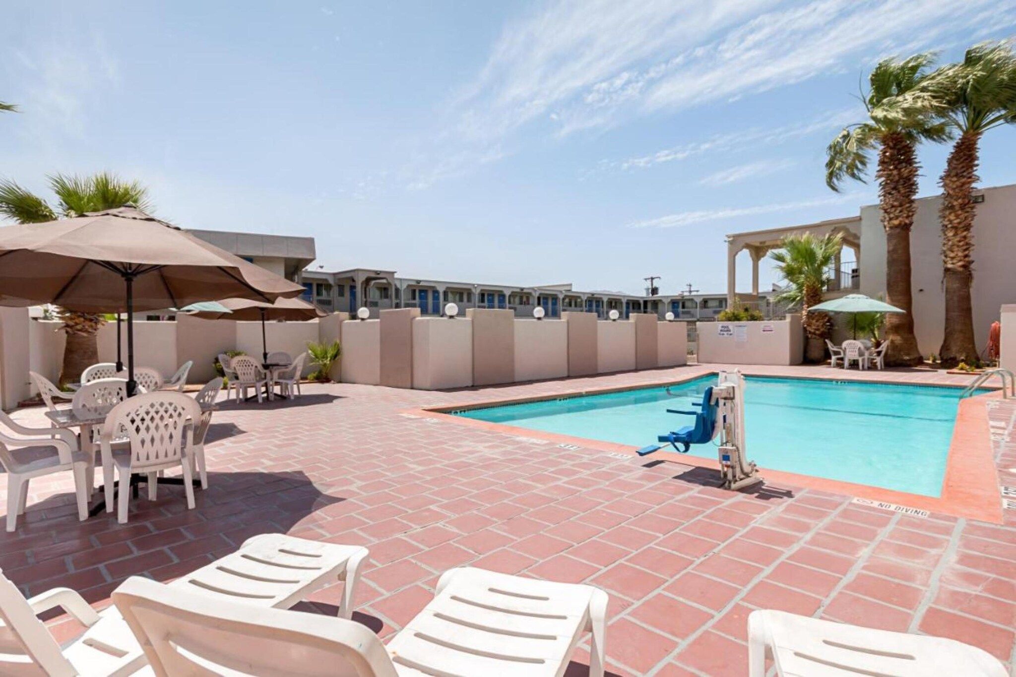 Un espace piscine avec des chaises longues et des parasols, un ciel dégagé et un bâtiment en arrière-plan.