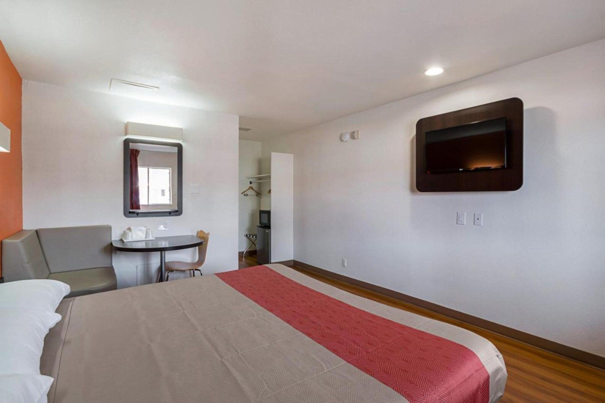 Habitación de hotel con cama, escritorio, silla, televisión y espejo.