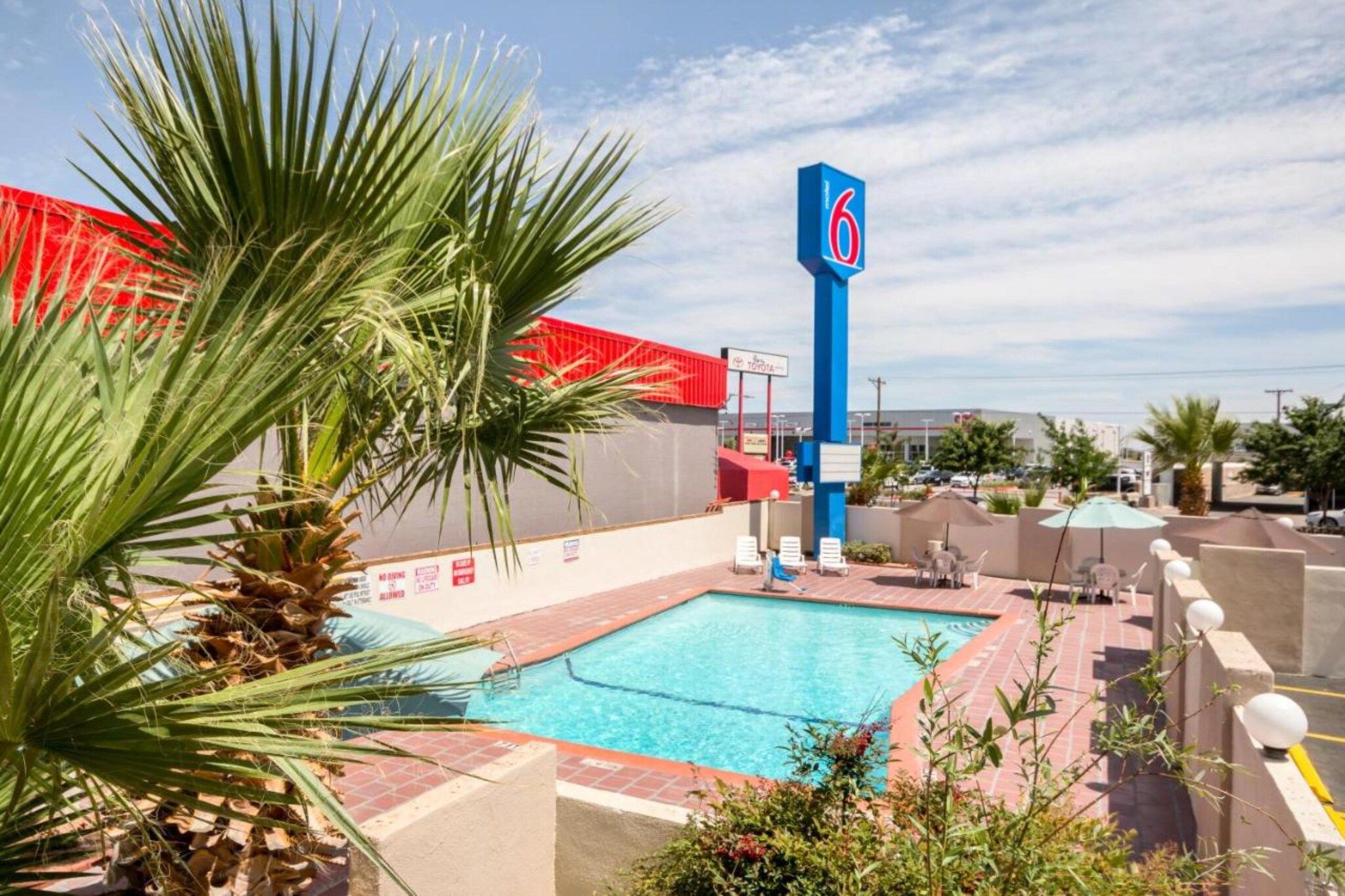 Une piscine avec un panneau bleu, des palmiers et un bâtiment rouge en arrière-plan.