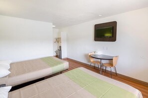 Habitación de hotel con dos camas individuales, un escritorio con silla y un televisor montado en la pared.
