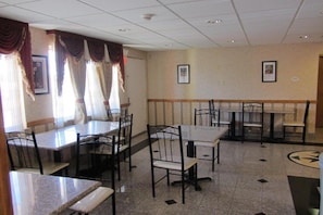 Een eethoek met tafels en stoelen, een betegelde vloer en een decoratieve wand.