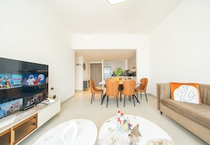 A modern living room with a flat-screen TV, a dining area with a table and chairs, and a sofa with decorative pillows. - Waterfront Apt w/ Pool, Gym & Direct Beach Access (Sharjah)