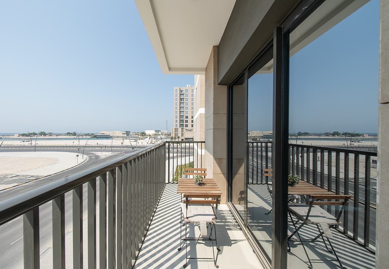 A balcony with a view of a road and buildings, furnished with a table and chairs.