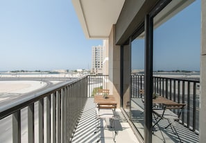 A balcony with a view of a road and buildings, furnished with a table and chairs. - Waterfront Apt w/ Pool, Gym & Direct Beach Access (Sharjah)