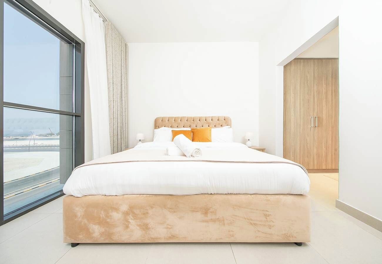 A modern bedroom with a large bed, a view through a window, and a wooden wardrobe.