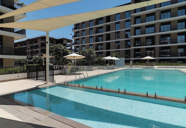 A swimming pool with a clear blue water surface, surrounded by a tiled deck area. - Waterfront Apt w/ Pool, Gym & Direct Beach Access (Sharjah)