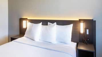 Habitación de hotel con una cama grande, ropa blanca, dos mesitas de noche con lámparas y un cabecero oscuro.