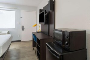 Et hotelværelse med seng, skrivebord, fjernsyn og mikroovn.