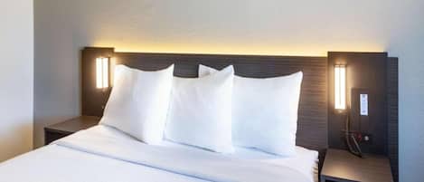 A hotel room with a large bed, white linens, two bedside tables with lamps, and a dark headboard.
