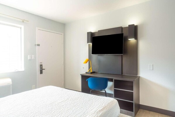 A hotel room with a bed, a desk with a chair, a flat-screen TV mounted on the wall, and a window. - 1 Queen Bed | Non-Smoking, Micfridge (Del Rio)