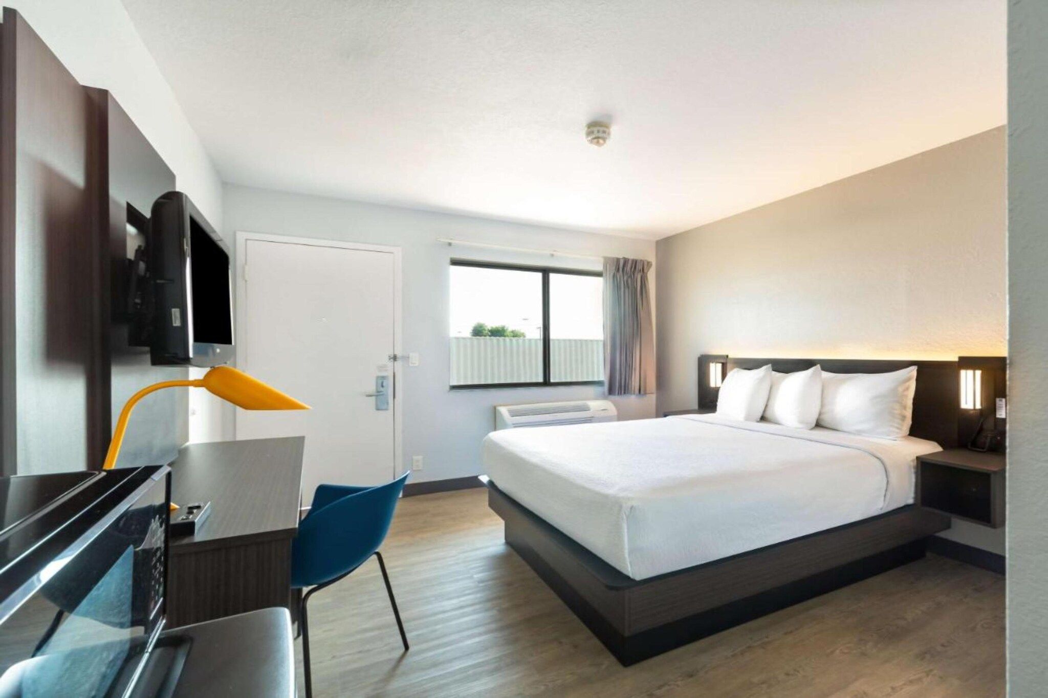 Una habitación de hotel con cama, escritorio, silla, televisor y ventana.