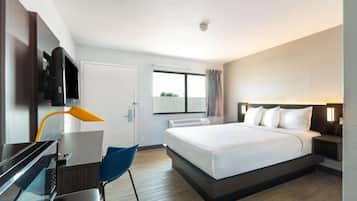 Una habitación de hotel con cama, escritorio, silla, televisor y ventana.