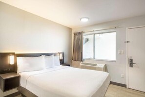 A hotel room with a bed, bedside tables, a window with curtains, an air conditioning unit, and a door. - ADA Queen Bed|RI Shower|Nsmk (Del Rio)
