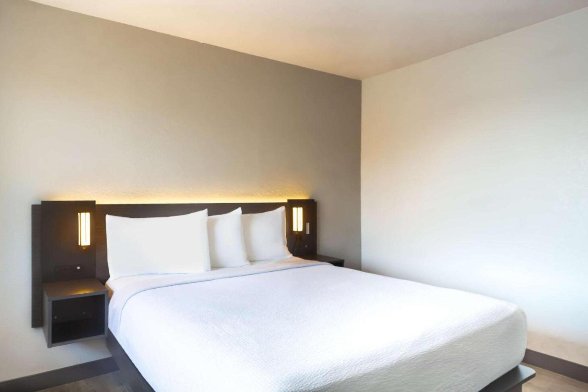 Habitación de hotel con una cama grande, dos mesitas de noche e iluminación en la pared.