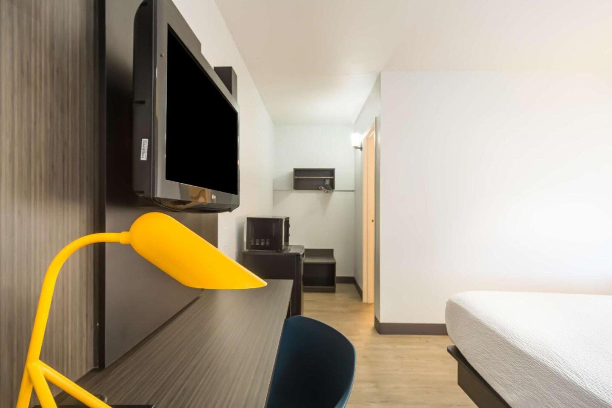 Quarto de hotel com cama, escrivaninha com luminária, televisão e pequena mesa com micro-ondas.