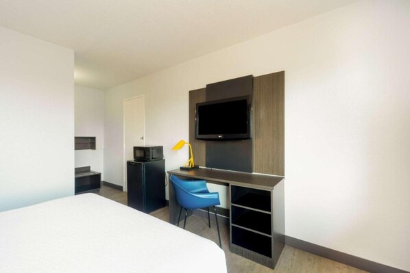Une chambre d’hôtel équipée d’un lit, d’un bureau avec une chaise, d’une télévision et d’un four à micro-ondes.