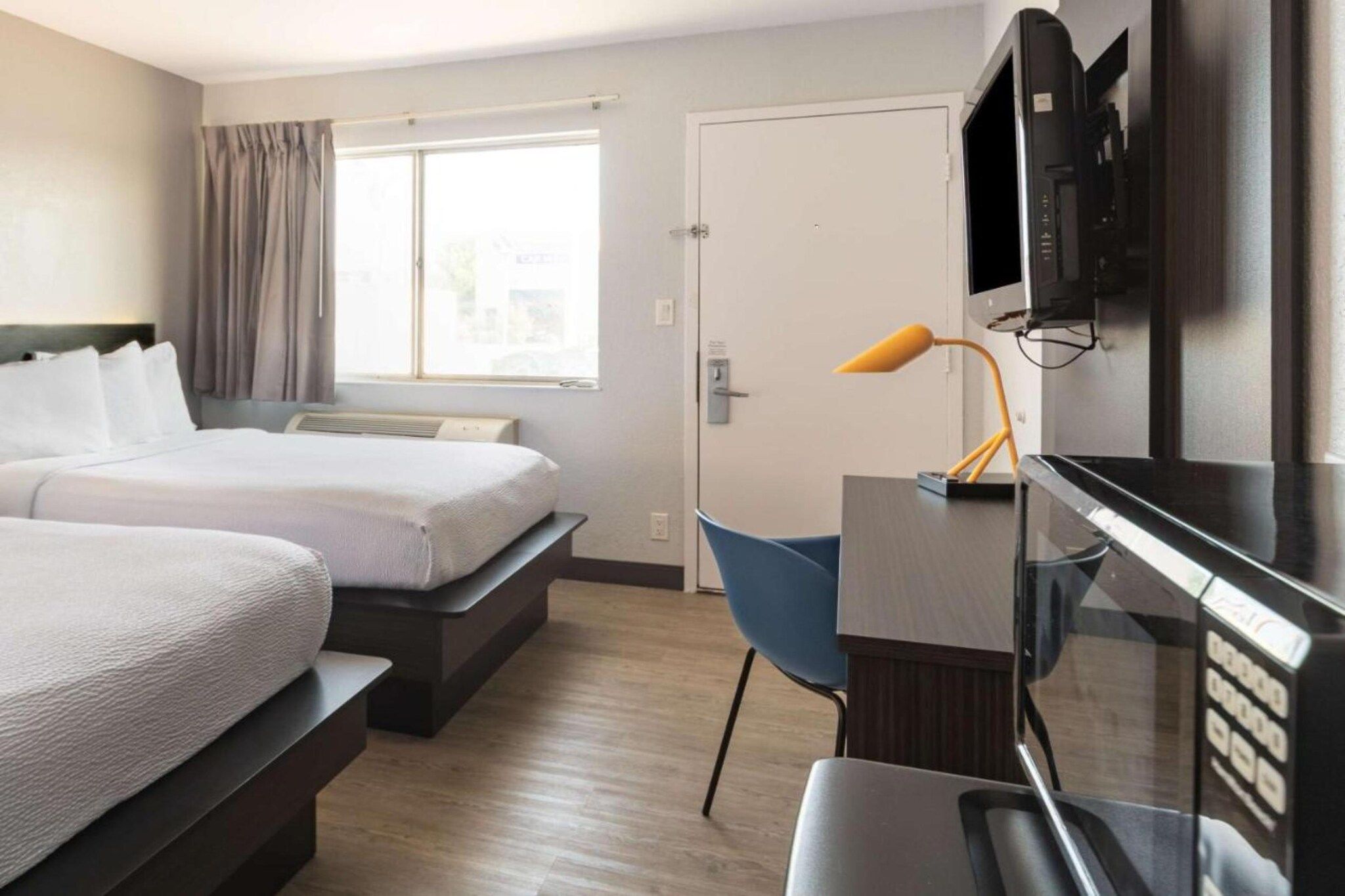 Habitación de hotel con dos camas, un escritorio, una silla, un televisor y un ventanal.