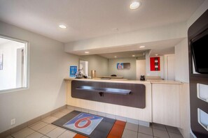 A hotel reception area with a counter, a digital screen, a red emergency exit sign, and a tiled floor with a number 6 sign. - 2 Full Beds | Non-Smoking (Del Rio)
