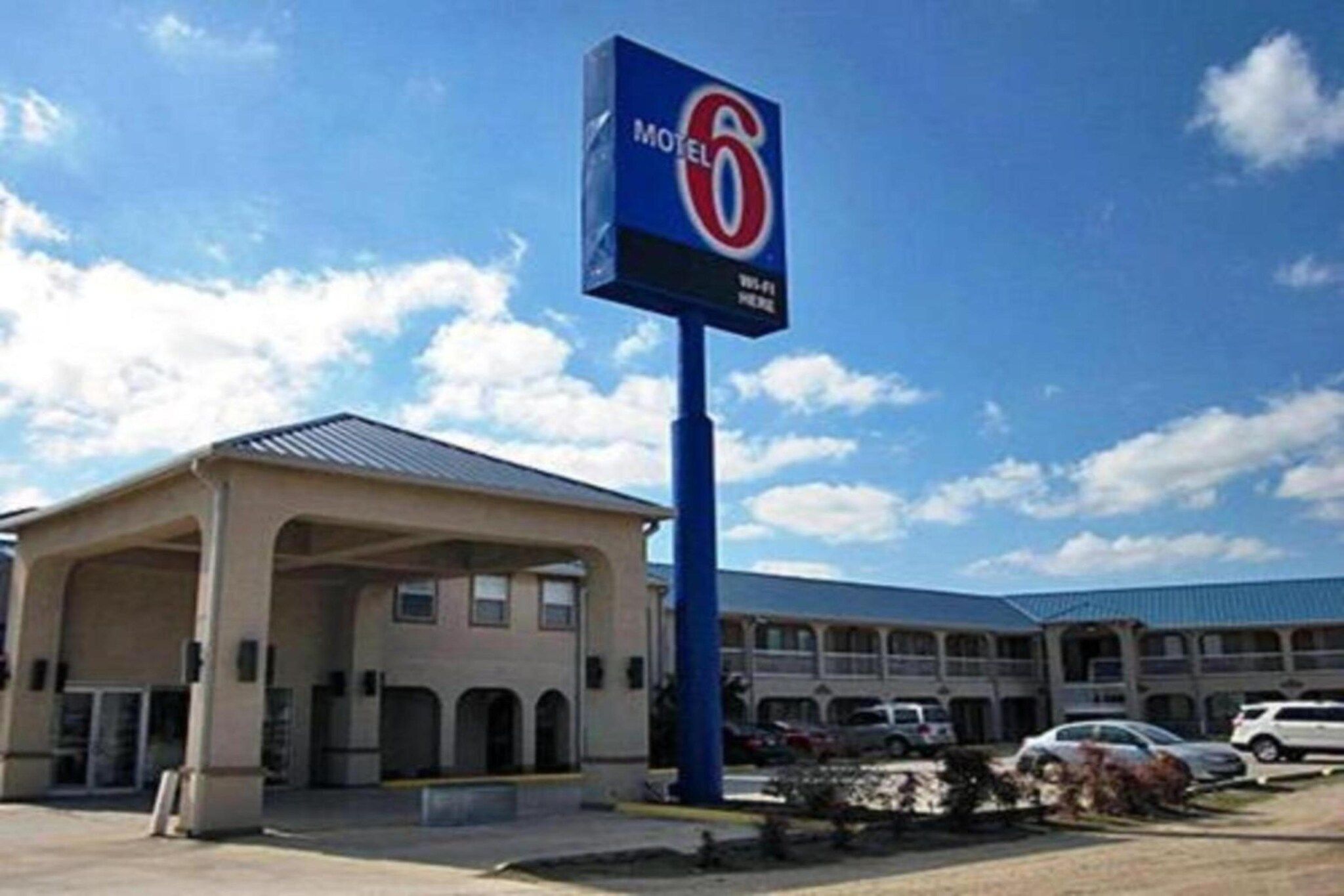 A motel with a prominent sign, a covered parking area, and a building with multiple windows.