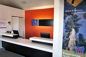 Een hotel receptiebalie met een groot nummer '6'-bord, een computer en een poster die het hotel promoot.