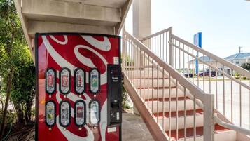 A Coca-Cola vending machine under a bridge with a staircase leading to a parking area.