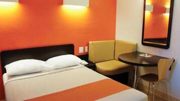 A hotel room with a bed, a chair, a small table, and a mirror.