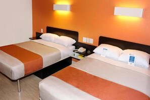 Two single beds with headboards, a bedside table with a lamp, and a wall-mounted light fixture. - 3 Queen Beds | Non-Smoking (Seguin)