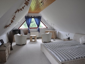 A bedroom with a sloped ceiling, a bed, two chairs, a small table, a nightstand, and a window with curtains. - Holiday Home With 5 Bedrooms (Ribnitz-Damgarten)